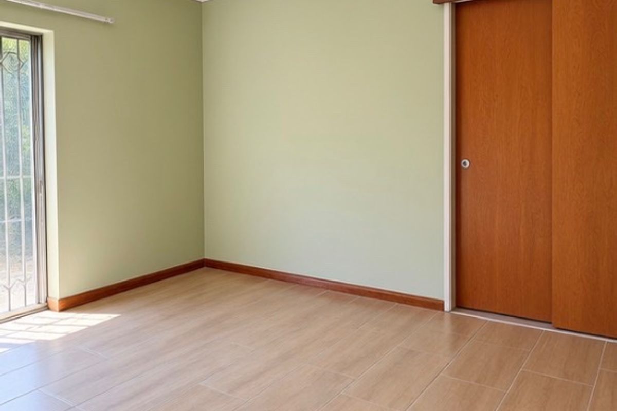 A bright, empty bedroom featuring light-toned tiled flooring, sage green walls, and a wooden sliding door.