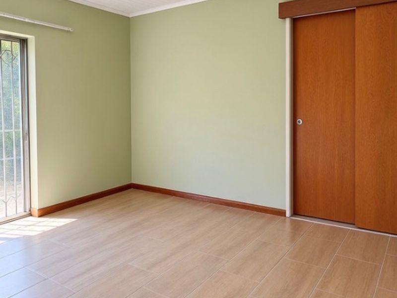 A bright, empty bedroom featuring light-toned tiled flooring, sage green walls, and a wooden sliding door.