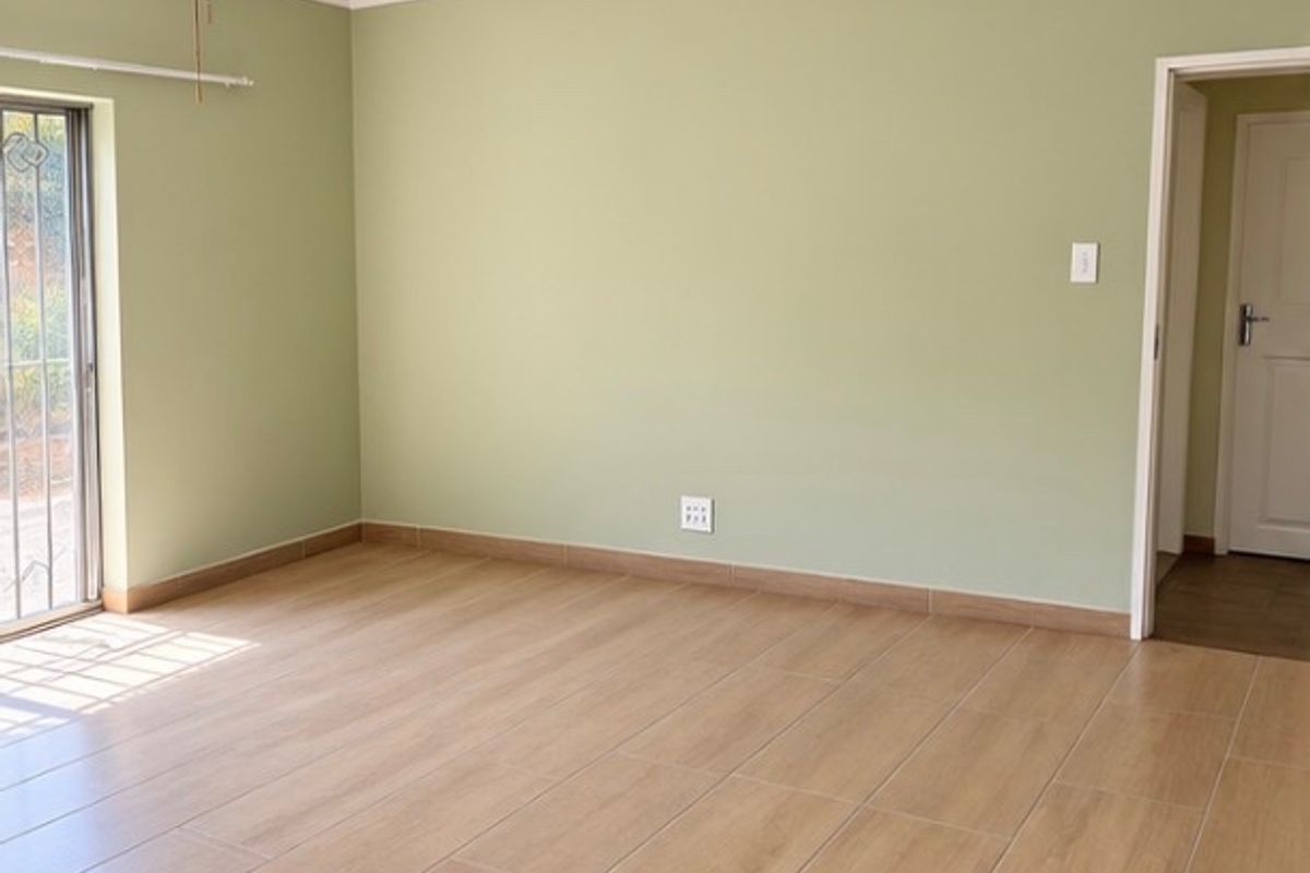 A bright, empty bedroom featuring light wood-look tiled flooring, sage green walls, a ceiling fan, and a sliding glass door with security gate.