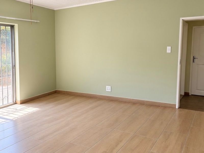 A bright, empty bedroom featuring light wood-look tiled flooring, sage green walls, a ceiling fan, and a sliding glass door with security gate.