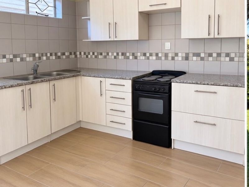 A clean, modern kitchen featuring light wood-finish cabinetry, granite countertops, a double sink, and a black freestanding stove with tiled backsplash.