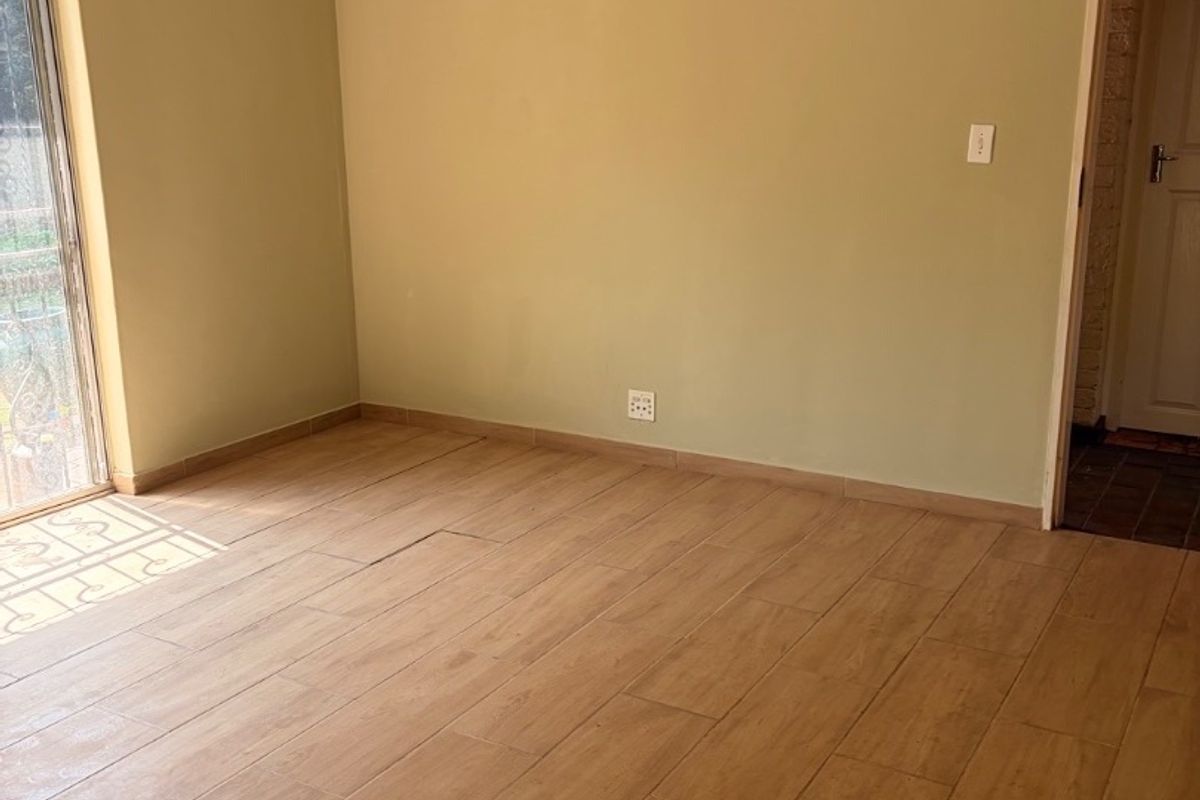 An empty living room featuring wood-look tiled flooring, a ceiling fan, and a sliding glass door providing natural light.