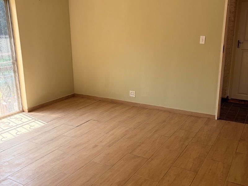 An empty living room featuring wood-look tiled flooring, a ceiling fan, and a sliding glass door providing natural light.