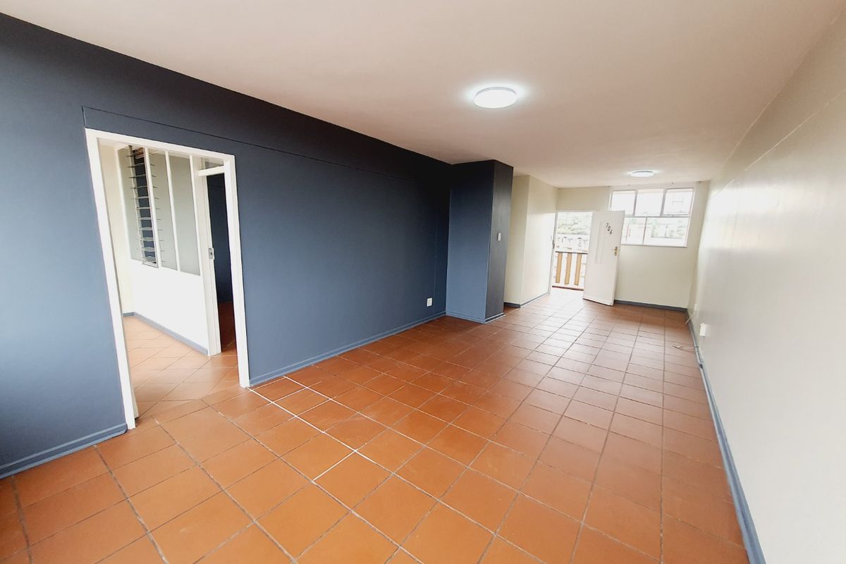 An empty living area featuring terracotta floor tiles, dark accent walls, and natural light from the external door and window.