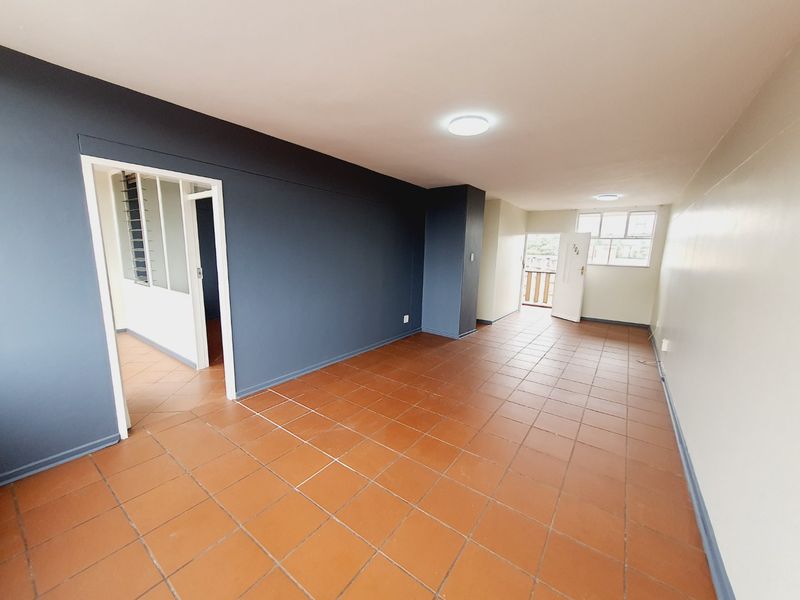 An empty living area featuring terracotta floor tiles, dark accent walls, and natural light from the external door and window.