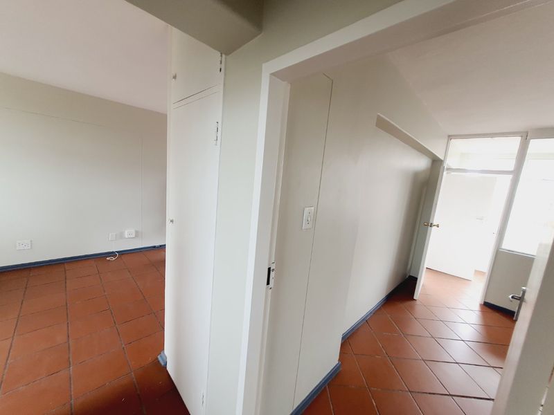 A bright, empty hallway featuring terracotta floor tiles, neutral walls, and a built-in storage cupboard, providing access to adjacent living spaces.