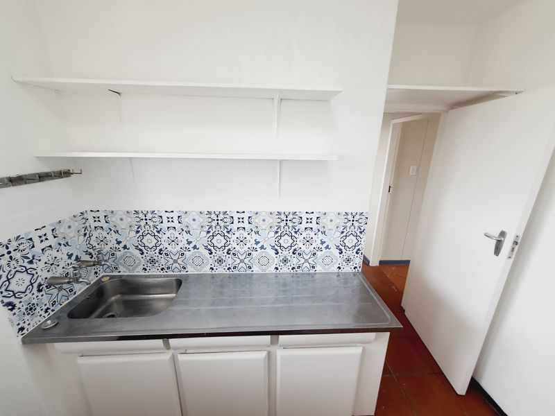 A functional scullery area featuring a stainless steel sink, decorative tiled splashback, built-in cabinetry, and open shelving for storage.
