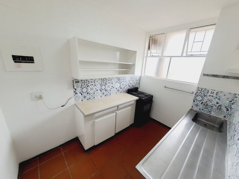 A functional kitchen featuring built-in cabinetry, a stainless steel sink, a freestanding stove, and decorative tiled backsplash with terracotta floor tiles.
