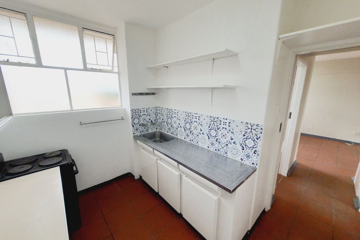 A compact kitchen featuring built-in cabinetry, a stainless steel sink, decorative tiled backsplash, and terracotta flooring, offering a functional layout for renovation.