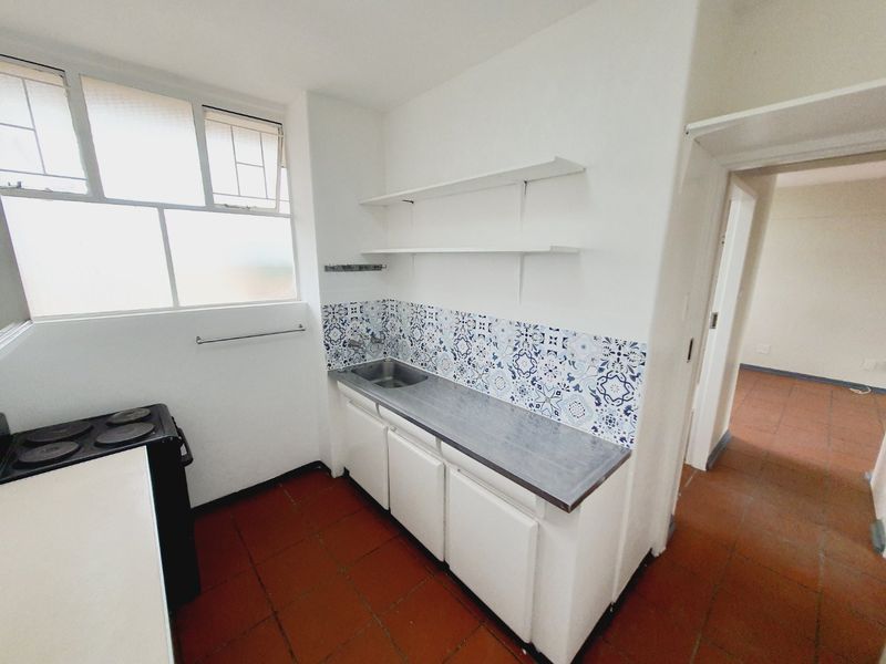 A compact kitchen featuring built-in cabinetry, a stainless steel sink, decorative tiled backsplash, and terracotta flooring, offering a functional layout for renovation.
