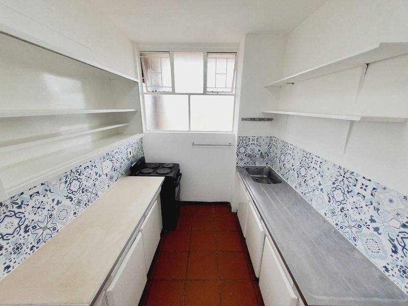 A compact, functional kitchen featuring built-in cabinetry, open shelving, a stainless steel sink, an electric stove, and decorative tiled backsplashes.