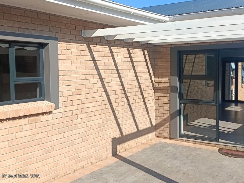 A clean, modern paved patio area featuring a white pergola, face-brick exterior walls, and dark aluminium window and door frames.