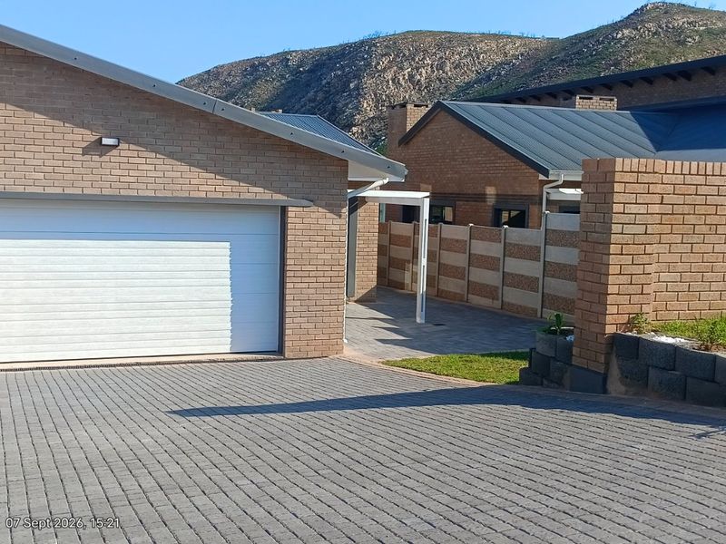 Front view of a modern brick house featuring a paved driveway, a white sectional garage door, and a neat garden area with mountain views.