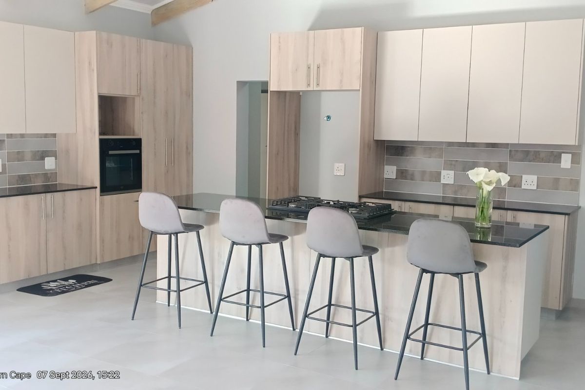 Modern kitchen featuring light wood-finish cabinetry, granite countertops, a central island with a gas hob, and a stylish tiled backsplash.