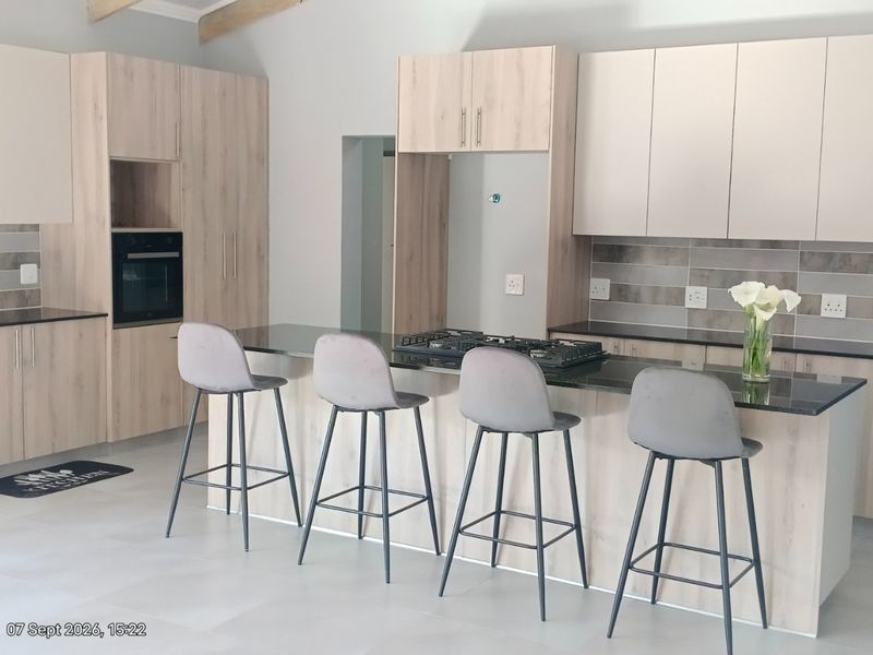 Modern kitchen featuring light wood-finish cabinetry, granite countertops, a central island with a gas hob, and a stylish tiled backsplash.