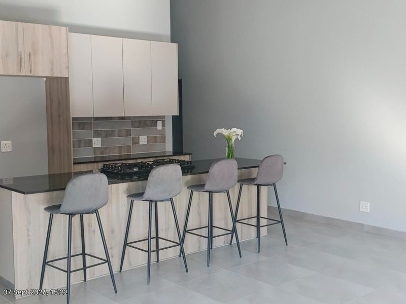Modern open-plan kitchen featuring light wood cabinetry, a dark stone breakfast bar with an integrated gas hob, and neutral tiled flooring.
