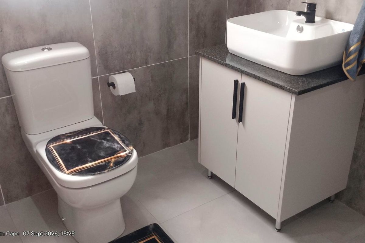 A modern bathroom featuring grey wall tiles, a white vanity cabinet with a vessel sink, and a standard toilet.