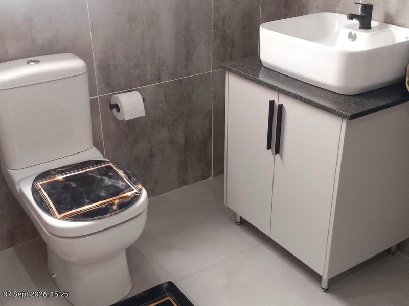 A modern bathroom featuring grey wall tiles, a white vanity cabinet with a vessel sink, and a standard toilet.