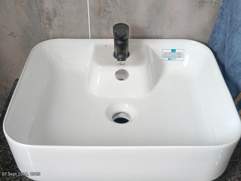 A modern white ceramic basin featuring a sleek black mixer tap, set against a contemporary tiled wall.
