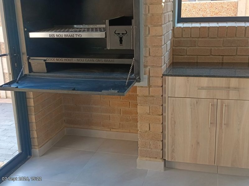 Covered patio area featuring a built-in braai, granite-topped cabinetry, and modern aluminium sliding doors leading to the outdoor space.