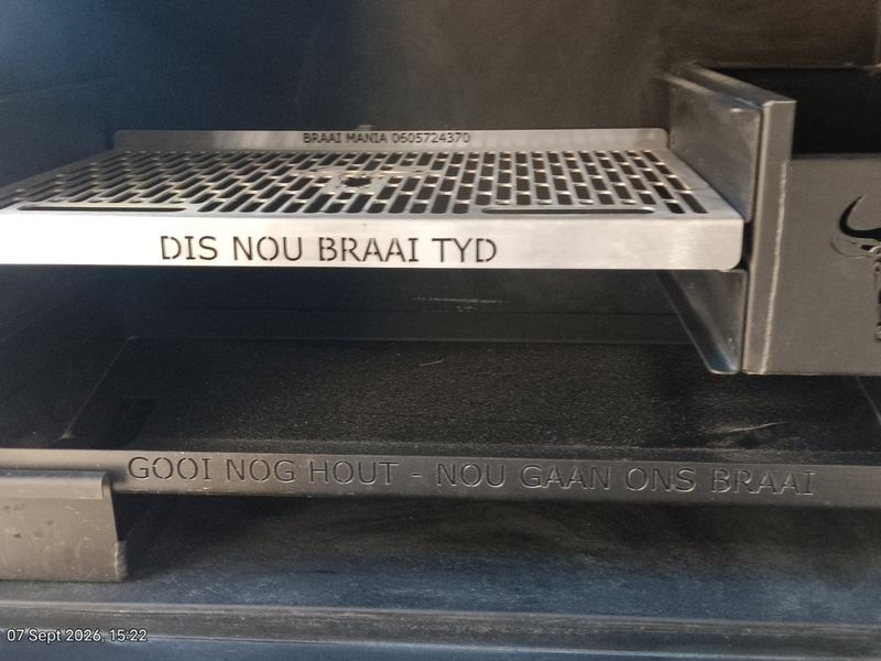 A close-up view of a clean, built-in steel braai unit featuring custom engraved metal grill and firebox components.