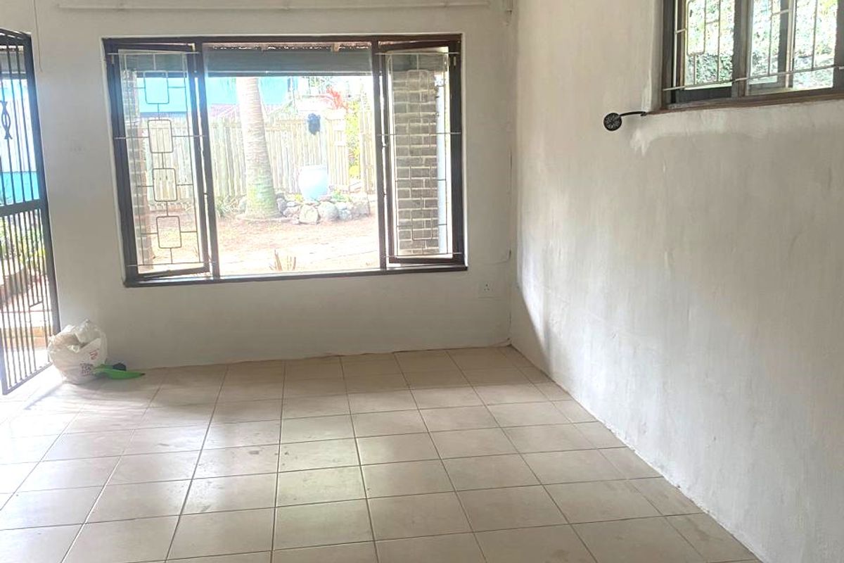 An empty living room featuring tiled flooring, security bars on the windows, and a security gate, presenting a blank canvas for renovation.
