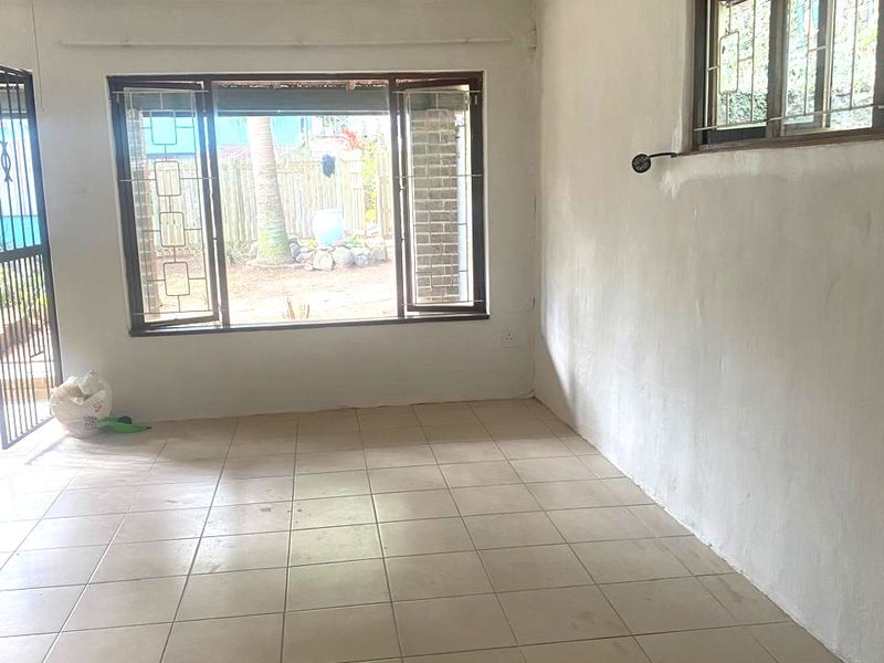 An empty living room featuring tiled flooring, security bars on the windows, and a security gate, presenting a blank canvas for renovation.
