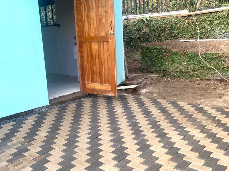 A rear exterior view featuring a newly laid herringbone paved patio, a timber entrance door with a protective awning, and a landscaped retaining wall.