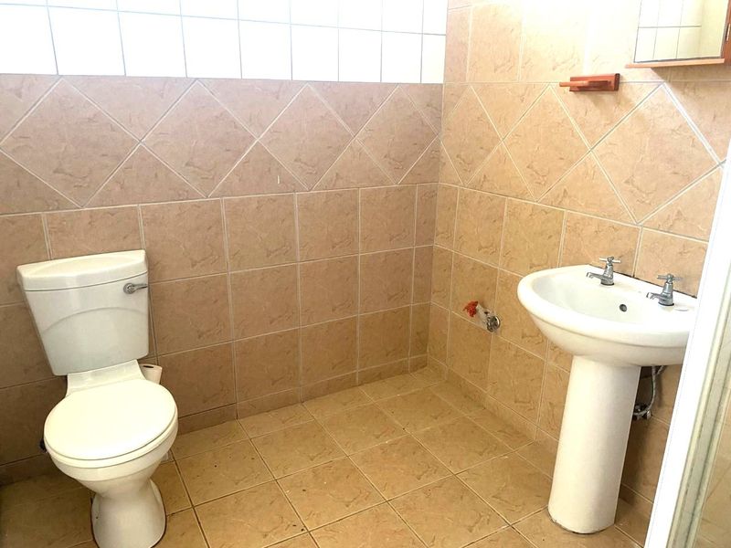A functional bathroom featuring a pedestal basin, toilet, and neutral ceramic tiling throughout, offering a clean and simple layout.