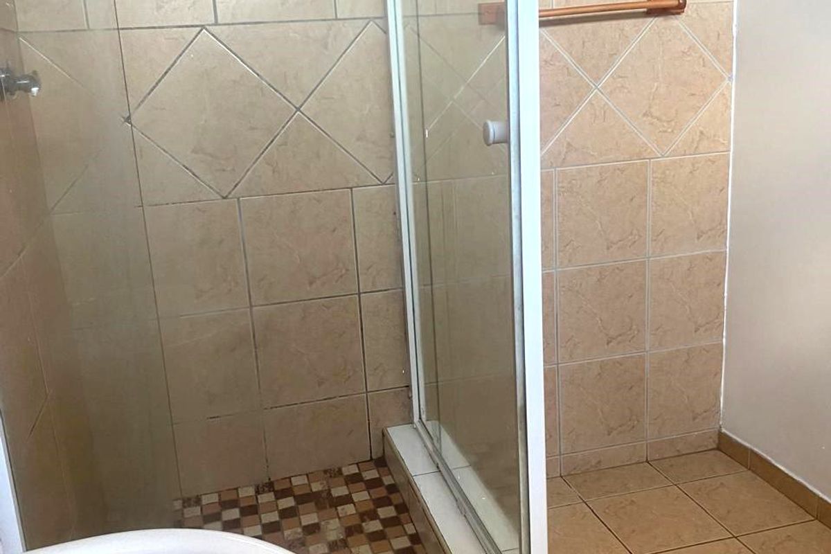 A functional bathroom featuring a glass shower enclosure with tiled flooring, a pedestal basin, and neutral wall tiling.