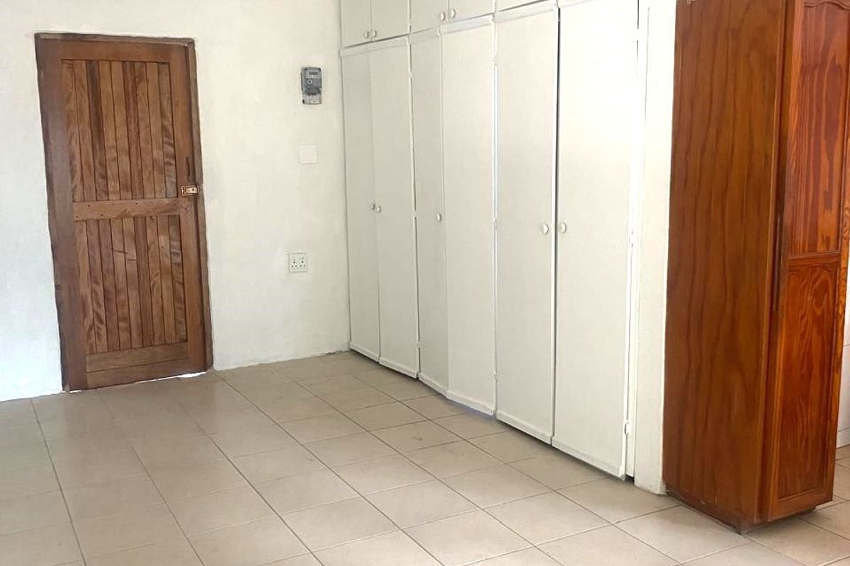 A vacant bedroom featuring built-in cupboards, tiled flooring, and a timber door. The room requires minor ceiling repairs and general cosmetic updates.