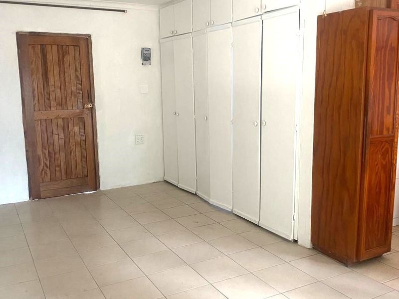 A vacant bedroom featuring built-in cupboards, tiled flooring, and a timber door. The room requires minor ceiling repairs and general cosmetic updates.