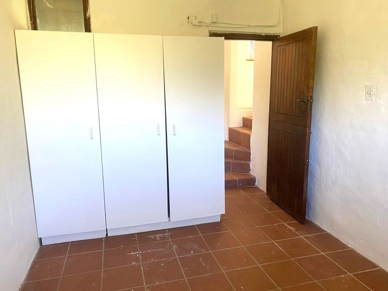 A simple bedroom featuring built-in wardrobes, tiled flooring, and direct access to a staircase area.