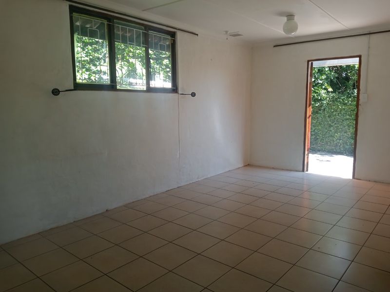 An empty living room featuring tiled flooring, a window with security bars, and direct access to the exterior.