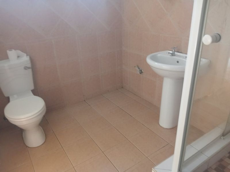 A functional bathroom featuring a pedestal washbasin, toilet, and shower enclosure with neutral ceramic wall and floor tiling.