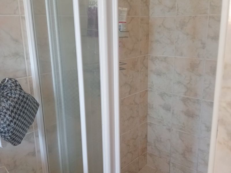 A functional shower stall featuring tiled walls and flooring, enclosed by a white-framed glass door.
