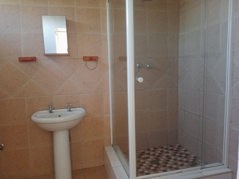 A functional bathroom featuring a pedestal basin and a glass-enclosed shower with tiled finishes throughout.