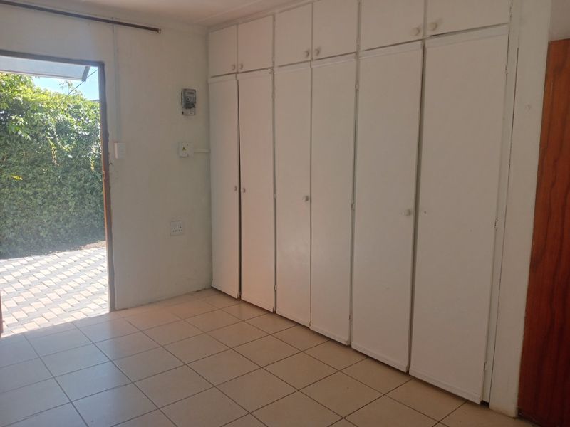 An empty bedroom featuring extensive built-in white cupboards, tiled flooring, and direct access to an outdoor paved area.