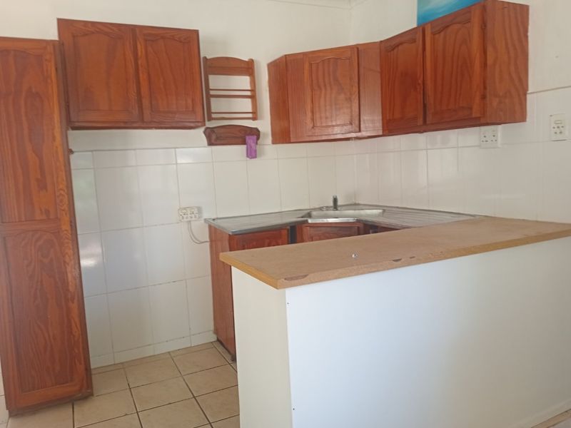 A functional kitchen featuring wooden cabinetry, a corner sink, tiled backsplash, and a breakfast bar counter, offering potential for modern updates.