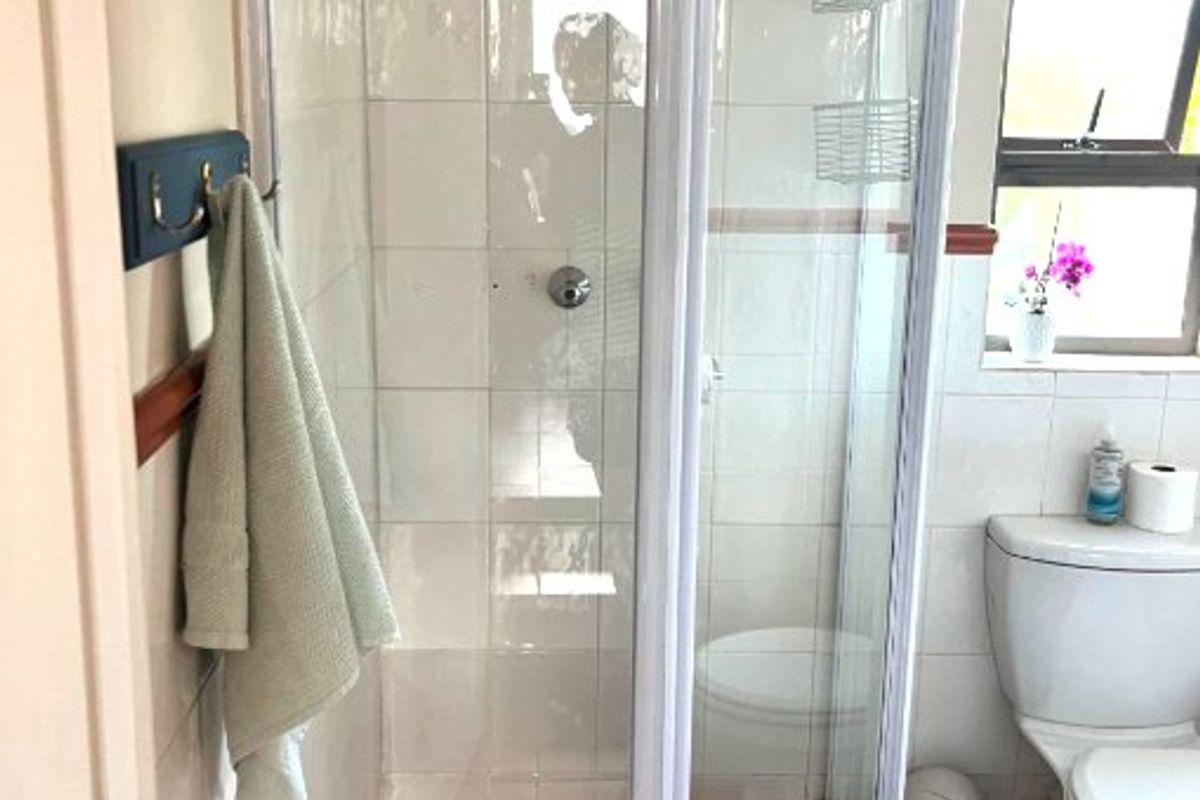 A functional bathroom featuring a corner shower enclosure with tiled walls and floor, alongside a standard toilet and window for natural light.