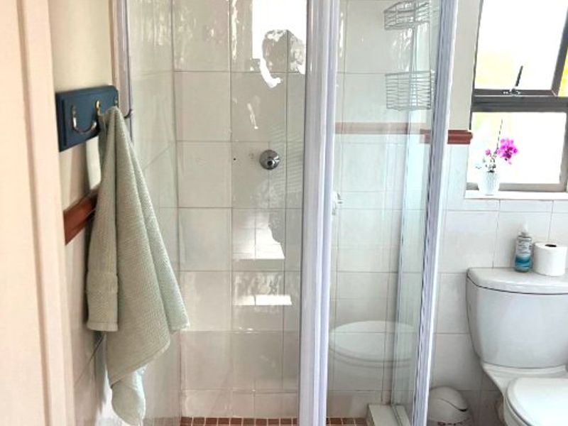 A functional bathroom featuring a corner shower enclosure with tiled walls and floor, alongside a standard toilet and window for natural light.