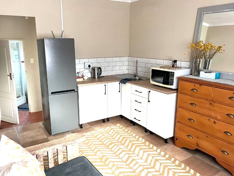A compact kitchen area featuring white cabinetry, a subway tile backsplash, laminate countertops, and a stainless steel sink, integrated into a living space.