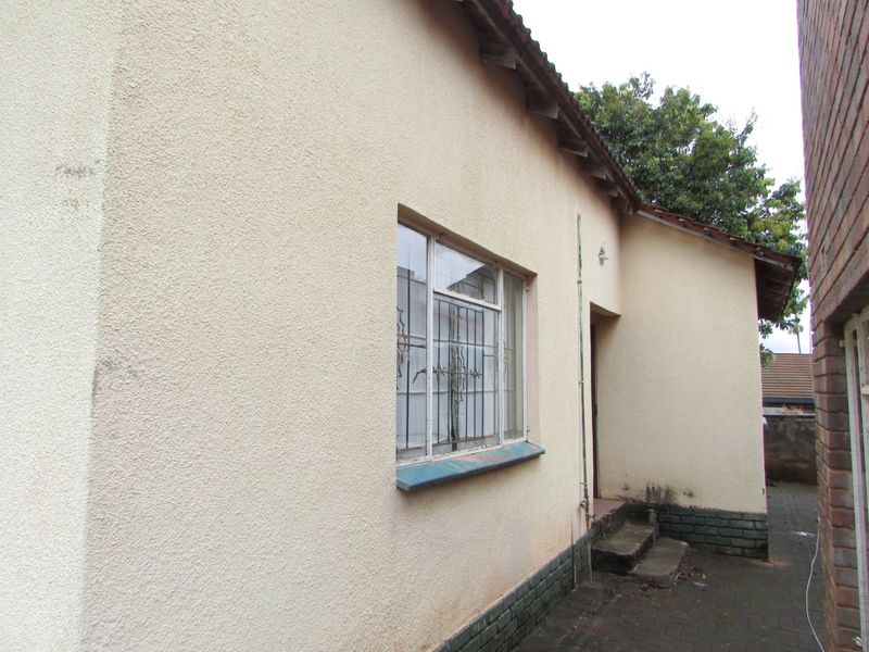 A side view of the property showing the exterior wall, metal security bars on the window, and concrete steps leading to the entrance.