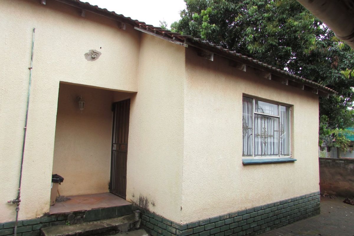 Rear exterior view of the house featuring a stucco facade, brick plinth, tiled roof, and a covered entrance with a security gate.