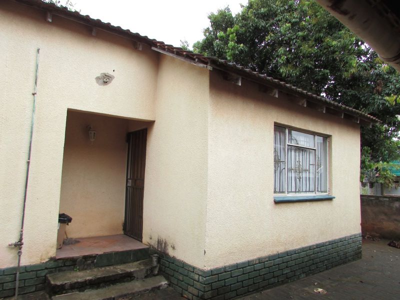 Rear exterior view of the house featuring a stucco facade, brick plinth, tiled roof, and a covered entrance with a security gate.