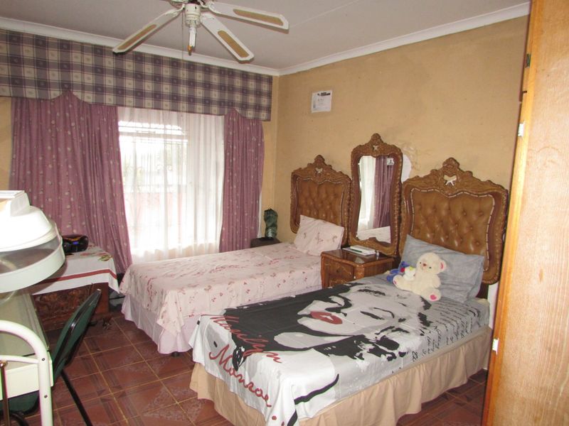 A bedroom featuring tiled flooring, a ceiling fan, and coved cornicing, currently showing signs of wear including peeling paint and damaged wall plaster.