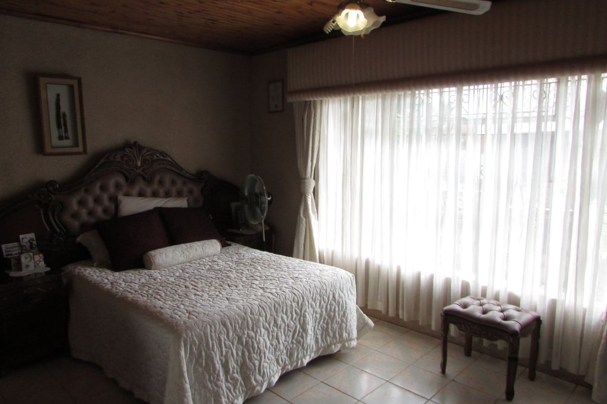A bedroom featuring a timber ceiling, ceiling fan, and tiled flooring, with large windows fitted with security bars.