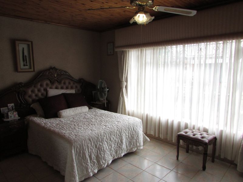 A bedroom featuring a timber ceiling, ceiling fan, and tiled flooring, with large windows fitted with security bars.