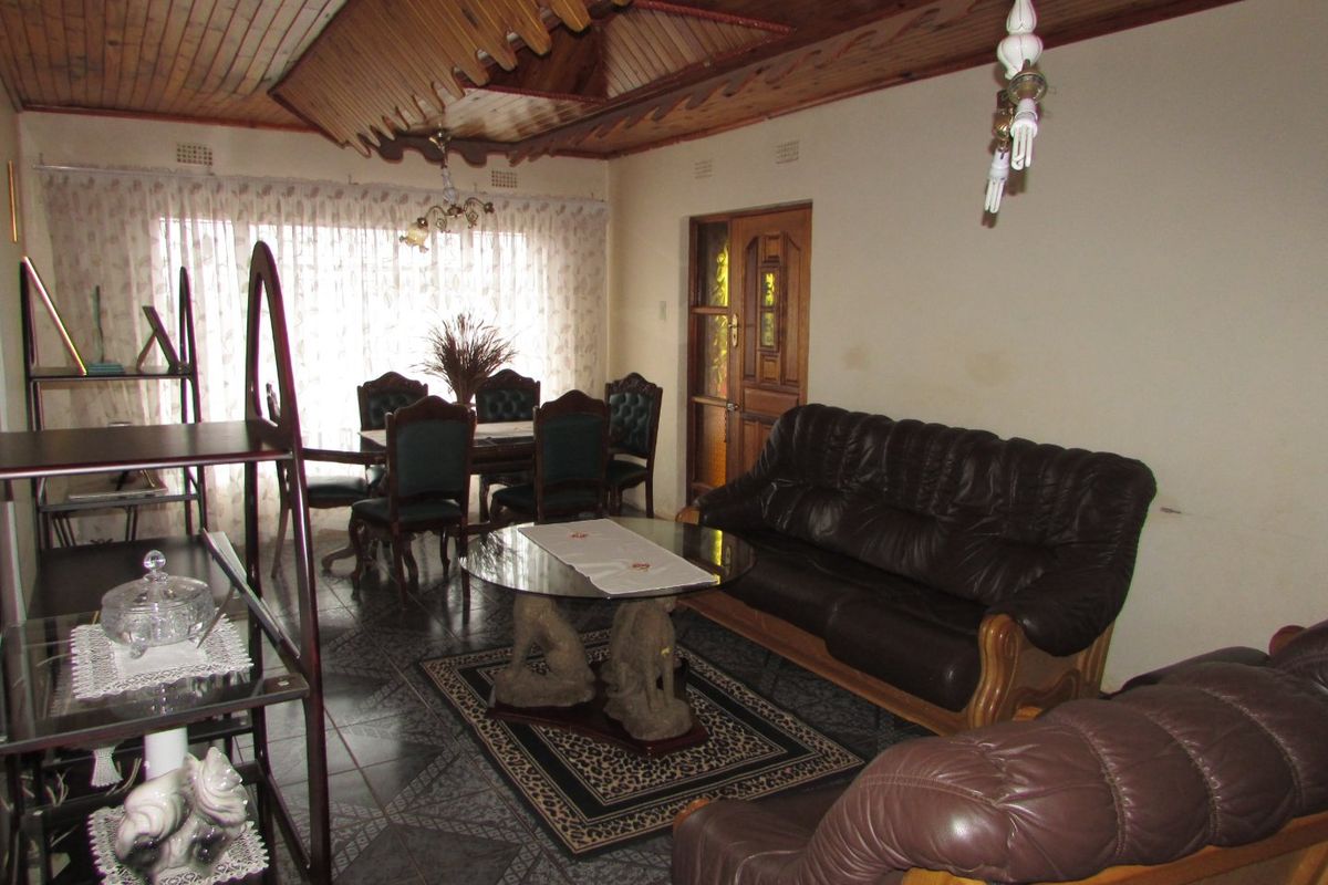 A living room featuring a distinctive timber-clad ceiling, tiled flooring, and a traditional timber-framed door, offering a dated aesthetic ready for modernization.