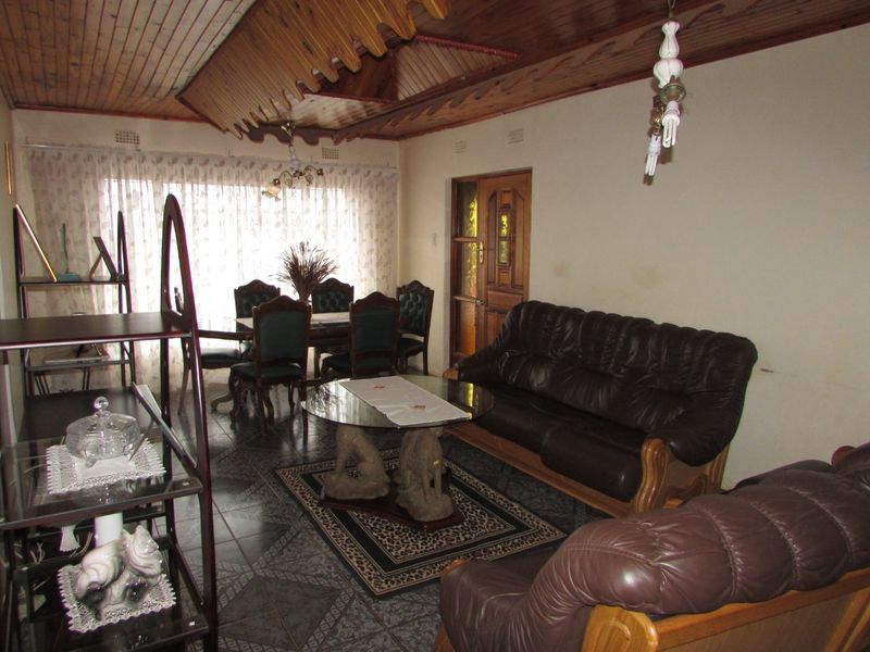 A living room featuring a distinctive timber-clad ceiling, tiled flooring, and a traditional timber-framed door, offering a dated aesthetic ready for modernization.